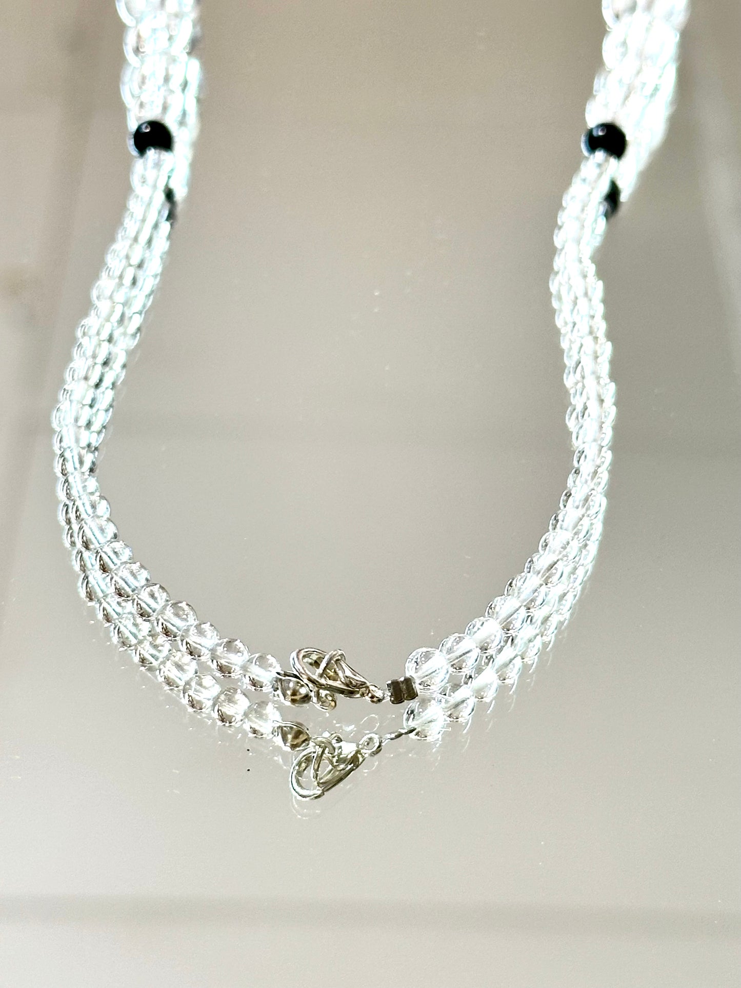 Multi-strand silver necklace with black beads on a light gray background