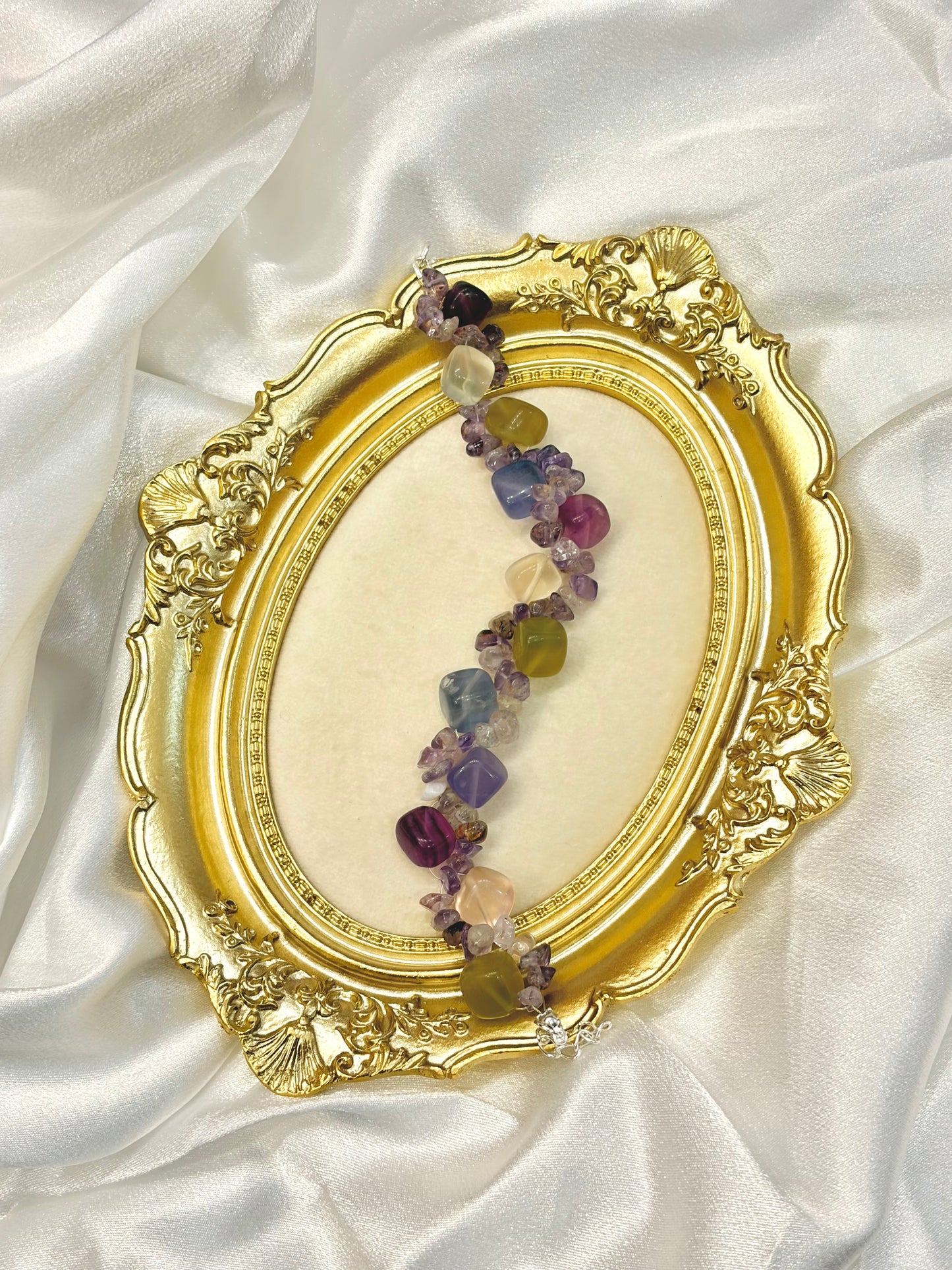 Multicolor fluorite and amethyst bracelet laid flat across gold ornate frame showing full length and adjustable chain