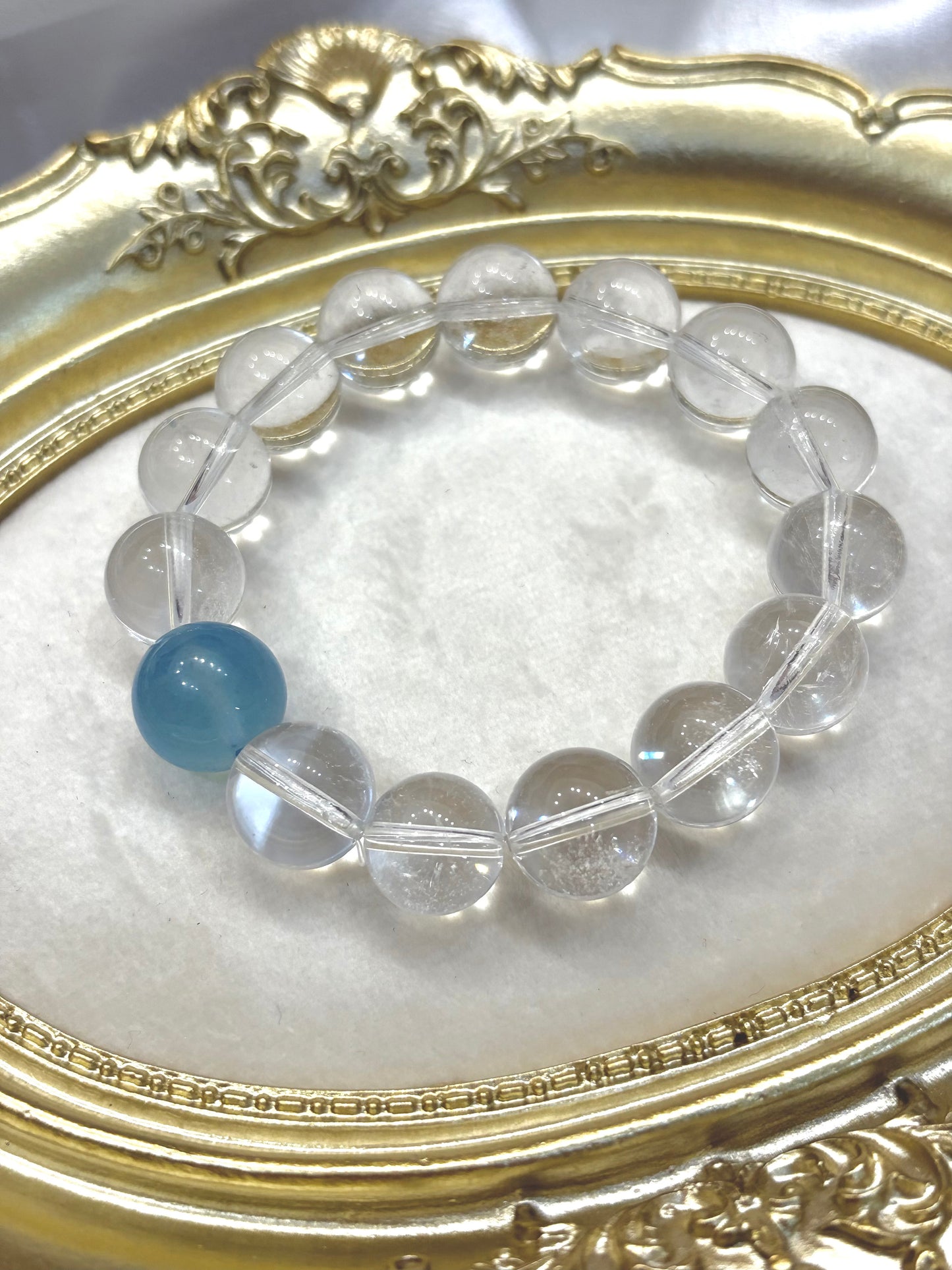 Clear quartz and aquamarine bracelet catching light in gold frame — transparent crystal beads with single blue stone centerpiece