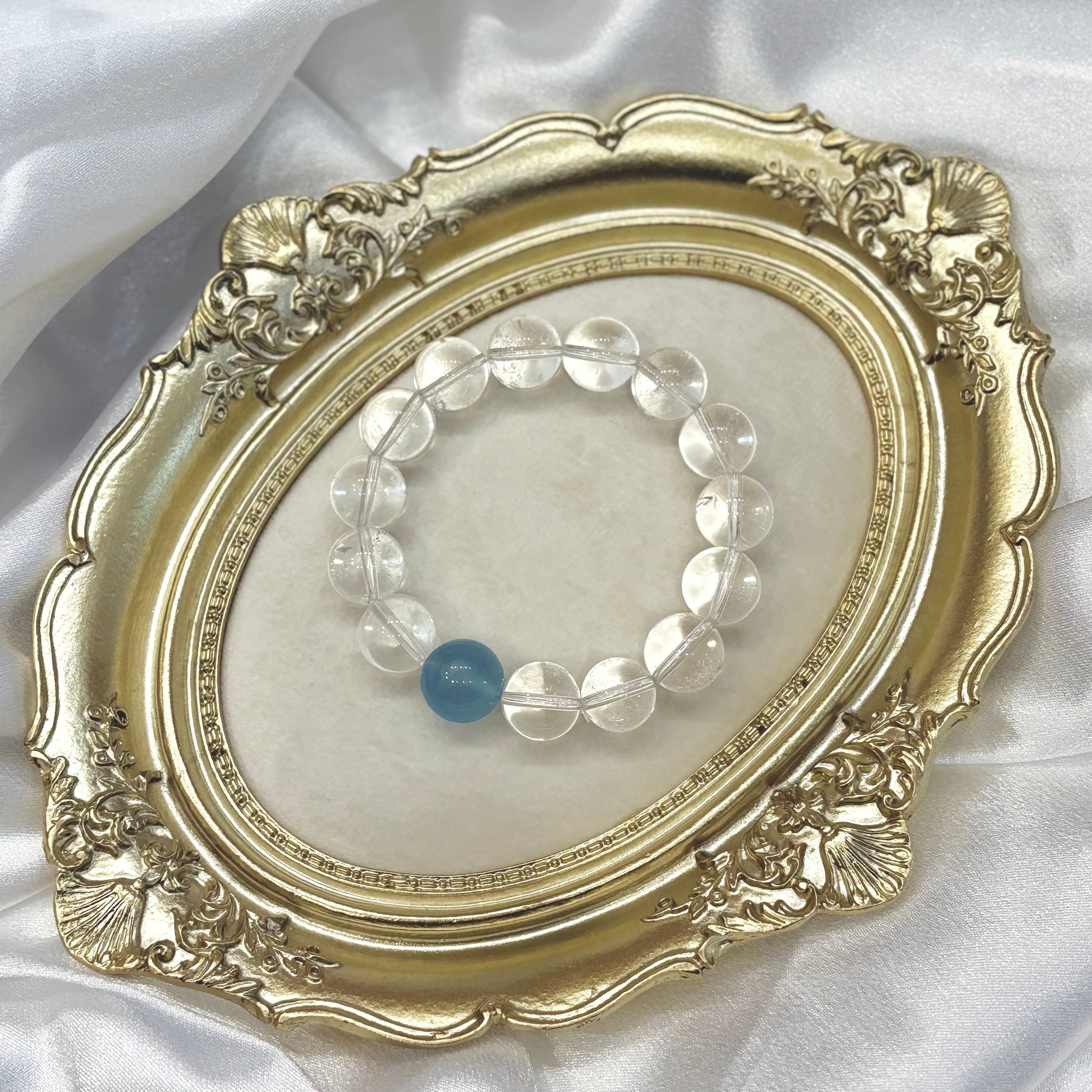 Handmade clear quartz bracelet with single aquamarine centerpiece displayed in gold ornate frame — minimalist healing crystal jewellery by XYD PLUS
