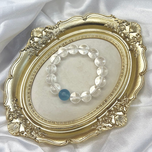 Handmade clear quartz bracelet with single aquamarine centerpiece displayed in gold ornate frame — minimalist healing crystal jewellery by XYD PLUS